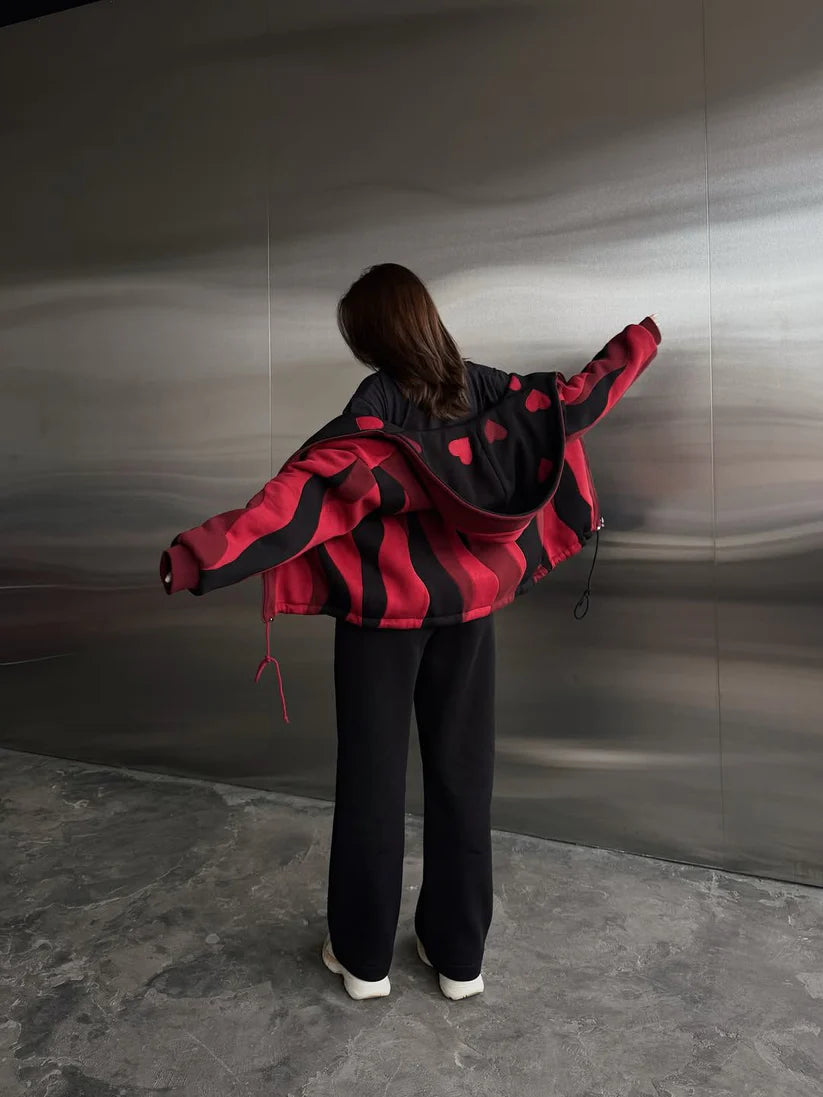 Person wearing a red and black jacket standing against a metallic wall.