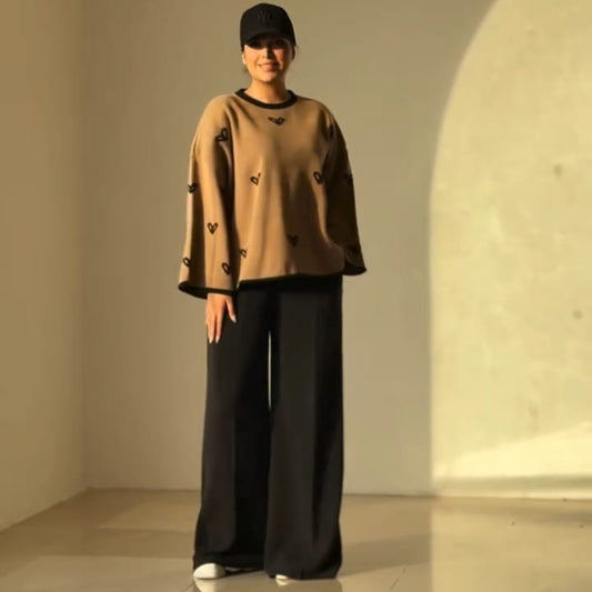 women wearing a camel heart printed winter top and black pants standing in a minimalistic room with a light-colored floor and wall.
