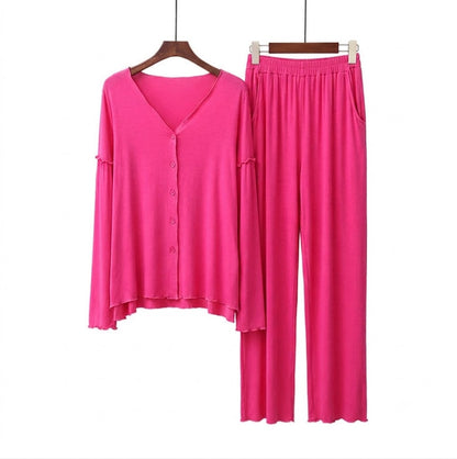 A two-piece women's lounge set in bright pink, featuring a long-sleeve button-front cardigan top and matching wide-leg pants, displayed on wooden hangers against a plain white background.