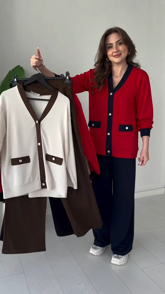 Woman holding a red cardigan with a white and brown outfit on a rack against a plain background