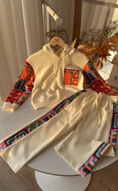 Beige hoodie and pants with colorful geometric patterns on a white surface.