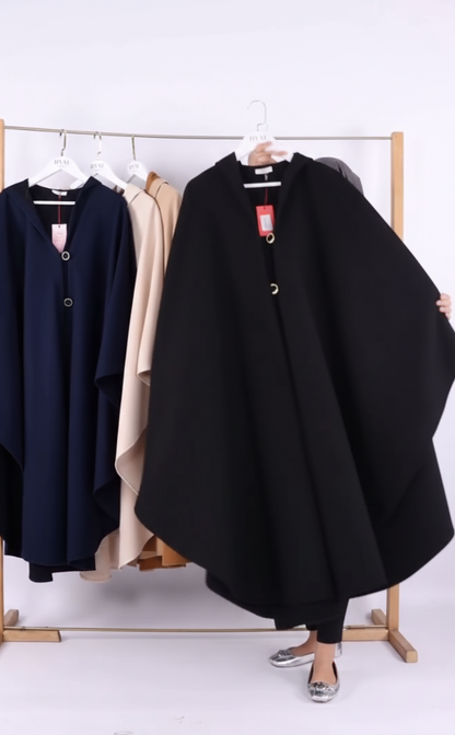 Black poncho on a rack with other clothing items against a white background