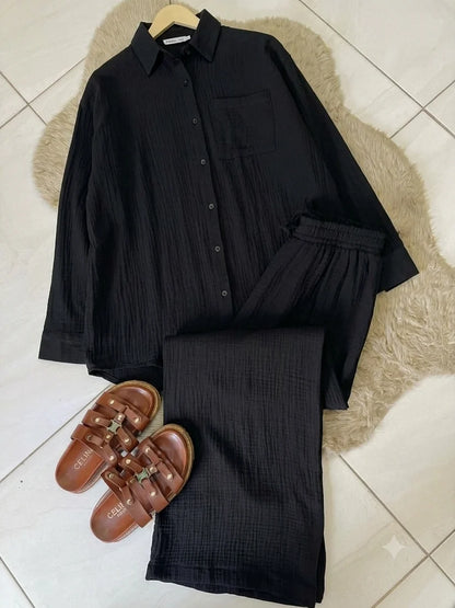 Chakoor textured two-piece pajama set consisting of a long-sleeve button-up shirt and matching pants, styled in a flat lay with black shoes and a black handbag on a brown faux fur rug over a tiled floor. 01