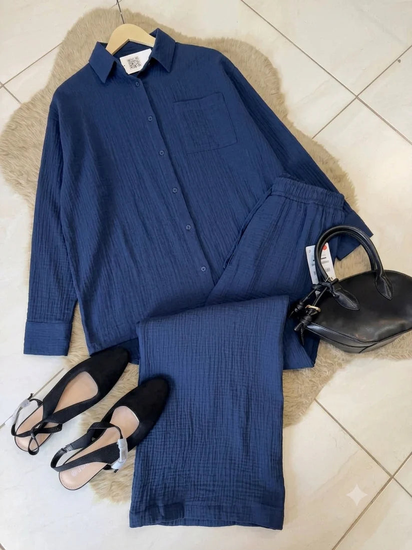 Chakoor textured two-piece pajama set consisting of a long-sleeve button-up shirt and matching pants, styled in a flat lay with black shoes and a black handbag on a brown faux fur rug over a tiled floor. 015