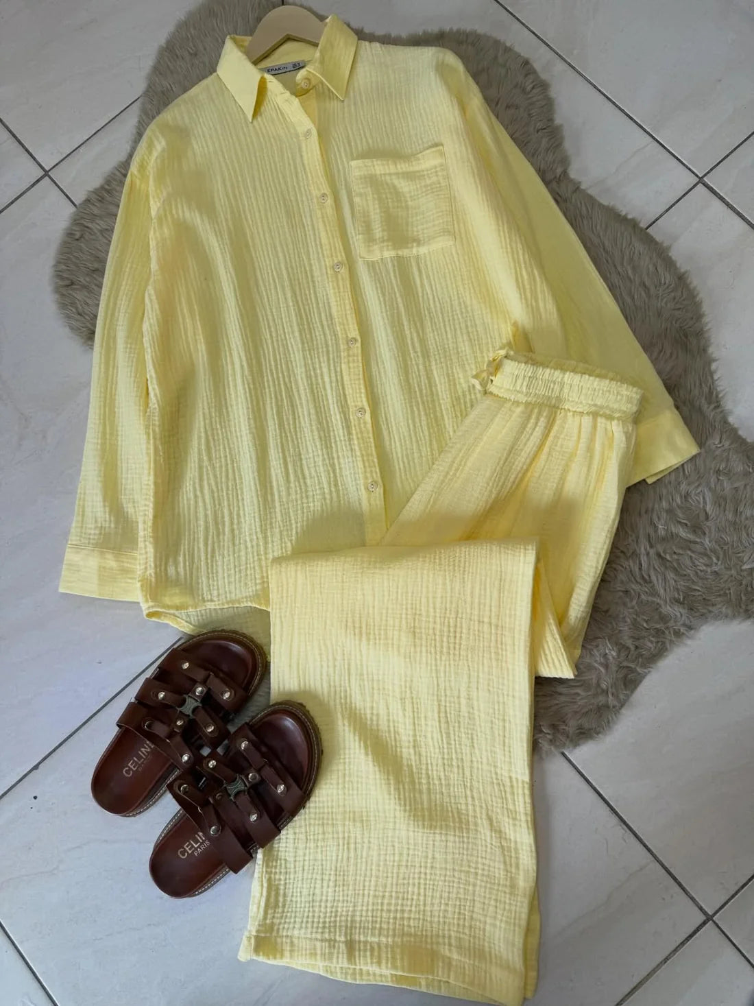 Chakoor textured two-piece pajama set consisting of a long-sleeve button-up shirt and matching pants, styled in a flat lay with black shoes and a black handbag on a brown faux fur rug over a tiled floor. 02
