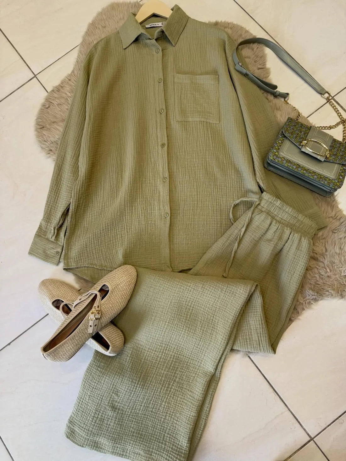Chakoor textured two-piece pajama set consisting of a long-sleeve button-up shirt and matching pants, styled in a flat lay with black shoes and a black handbag on a brown faux fur rug over a tiled floor. 06