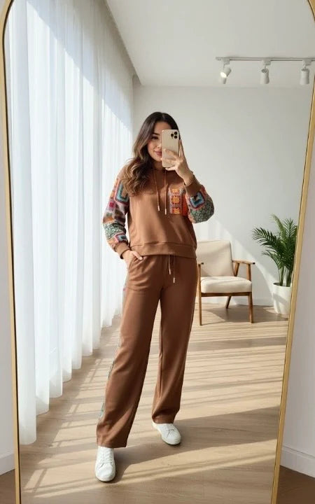Chakoor women taking a mirror selfie wearing a brown sweatshirt and pants in a bright room.