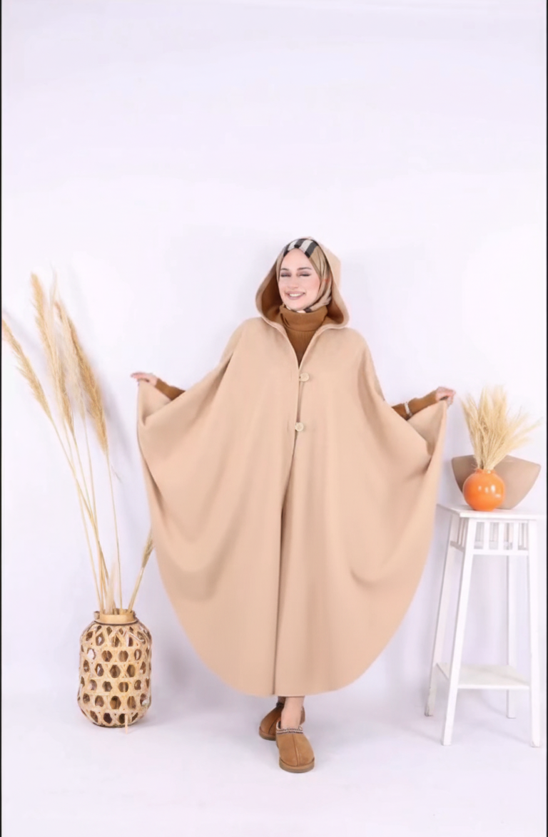 Person wearing a beige poncho in a minimalistic setting with a white background