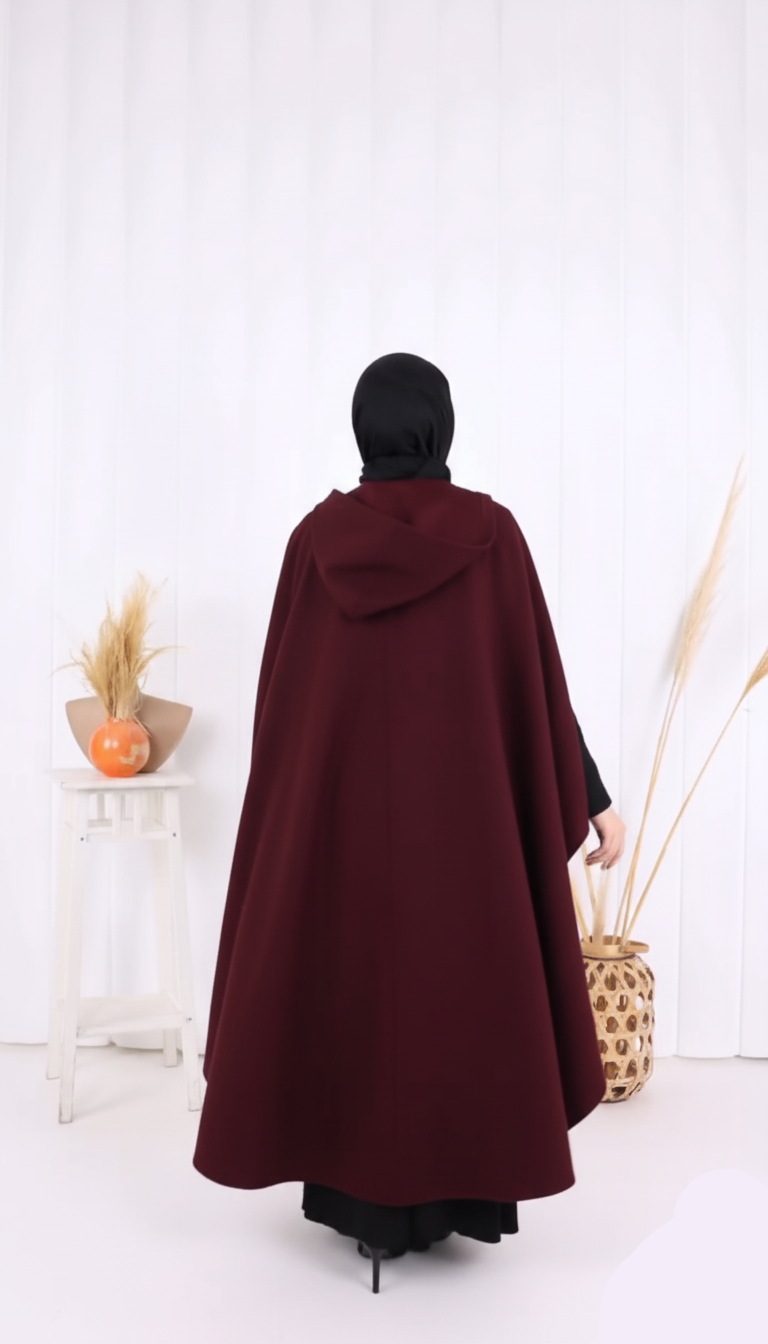 Person wearing a burgundy cloak with a hood in a minimalistic setting.