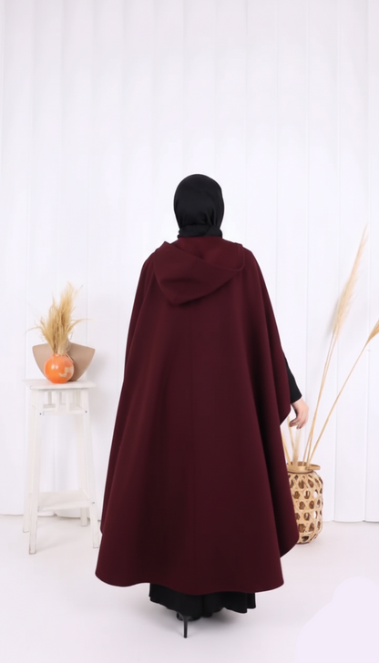 Person wearing a burgundy cloak with a hood in a minimalistic setting.