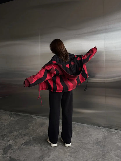 Person wearing a red and black jacket standing against a metallic wall.