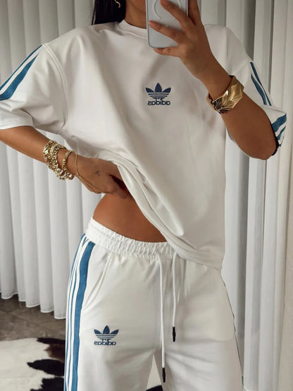 Stylish woman in black oversized co-ord set with striped track pants, sitting indoors and taking a mirror selfie. 06