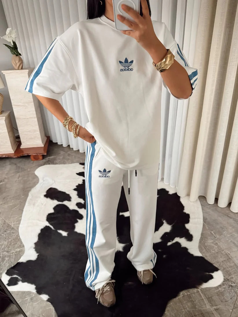 Stylish woman in black oversized co-ord set with striped track pants, sitting indoors and taking a mirror selfie. 07