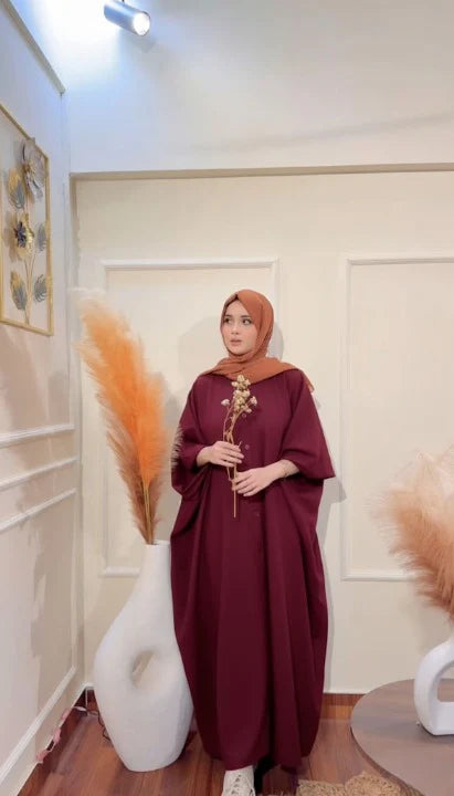 Woman in a burgundy dress holding a flower in a room with decorative elements.
