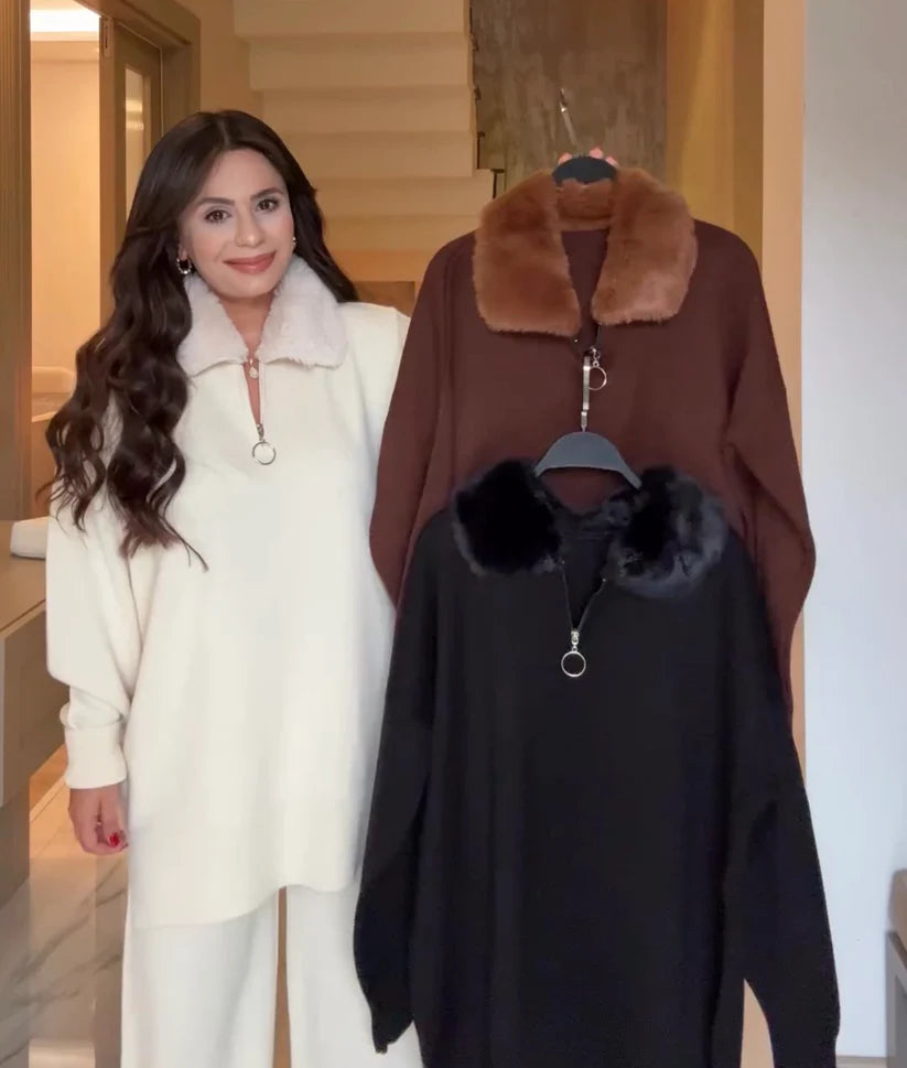 Woman standing next to two coats with fur collars, one white, one brown, and one black.