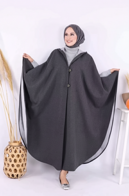 Woman wearing a black cape over a light gray outfit on a white background