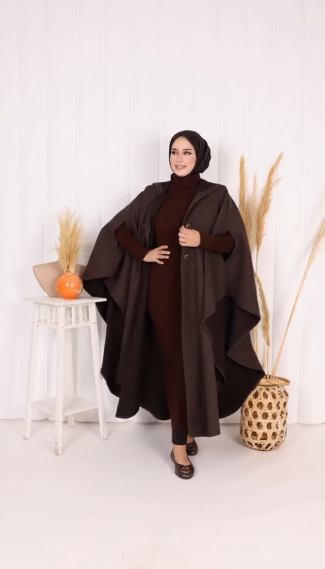 Woman wearing a dark brown abaya in a minimalistic setting with white walls and decorative elements.