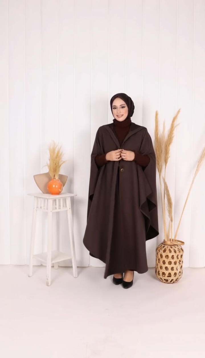 Woman wearing a long brown coat standing in a minimalistic room with decorative elements.