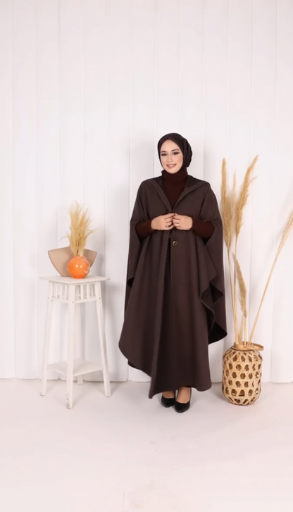 Woman wearing a long brown coat standing in a minimalistic room with decorative elements.