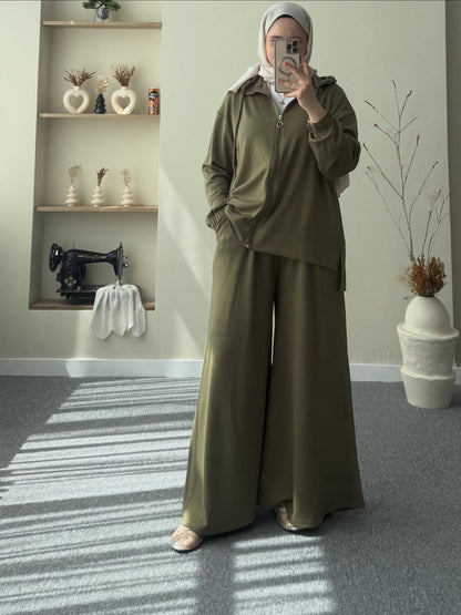 women taking a mirror selfie wearing an olive green outfit in a room with a sewing machine and shelves.