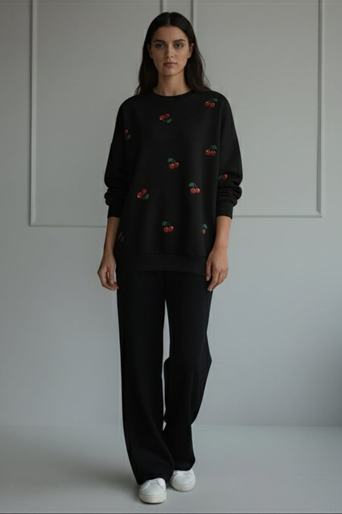 women wearing a black sweater with small red and yellow patterns and black pants, standing against a plain background. winter 2026