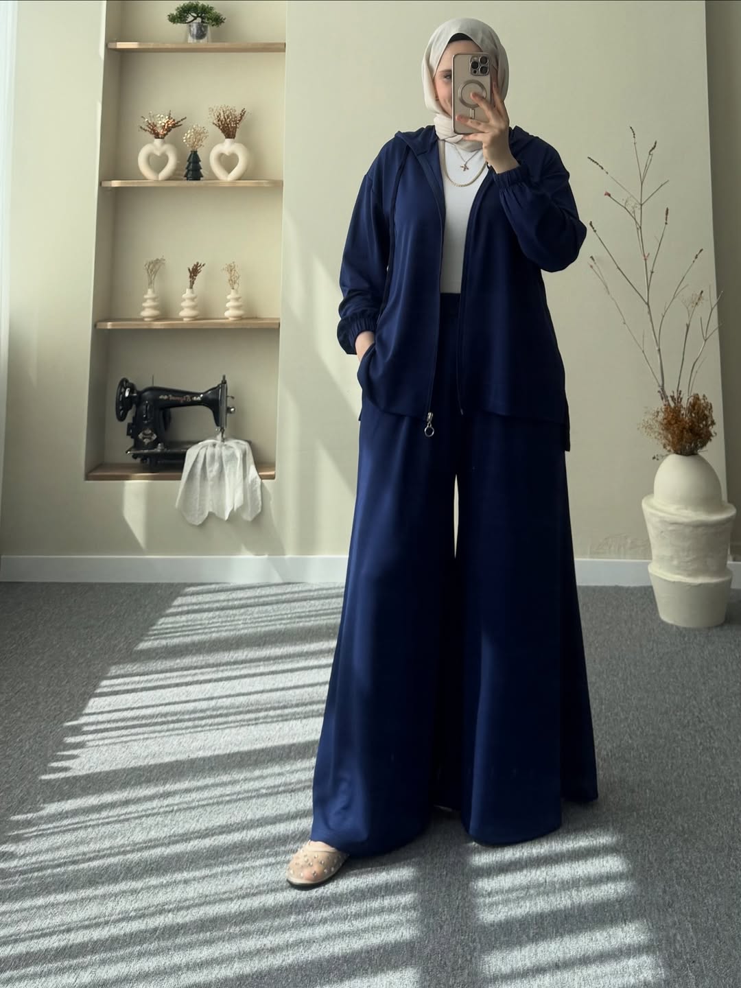women wearing a navy blue outfit taking a mirror selfie in a room with shelves and decor.