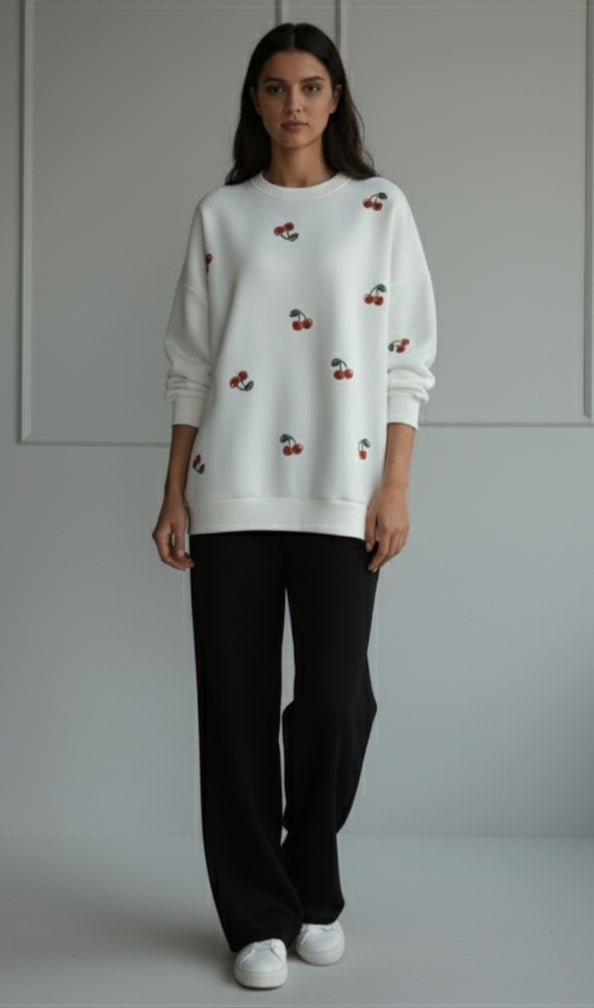 women winter 2026 wearing a white sweater with cherry pattern and black pants on a plain background