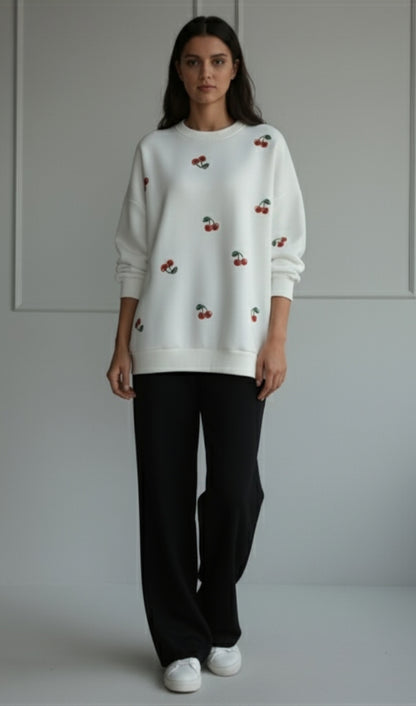 women winter 2026 wearing a white sweater with cherry pattern and black pants on a plain background